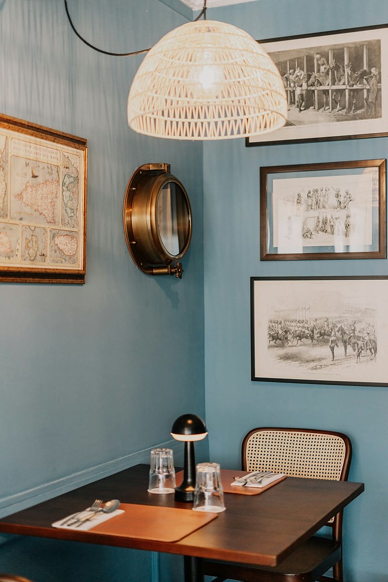 Dining corner with framed prints and a brass porthole on a blue wall